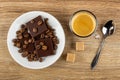 Coffee beans, pieces of chocolate in saucer, cup with coffee espresso, sugar cubes, spoon on wooden table. Top view Royalty Free Stock Photo