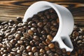 Coffee beans are poured from a Cup on a wooden background. Royalty Free Stock Photo
