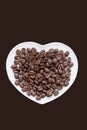 Coffee beans are poured on white plate in shape of heart. Brown background isolated Royalty Free Stock Photo