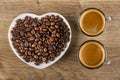 Coffee beans in saucer in heart shape, transparent cups with black coffee on wooden table. Top view Royalty Free Stock Photo