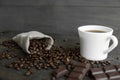 Coffee beans scattered from a linen bag on a wooden table. Cup of coffee and bar of dark chocolate. Mug of black coffee Royalty Free Stock Photo