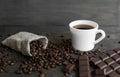 Coffee beans scattered from a linen bag on a wooden table. Cup of coffee and bar of dark chocolate. Mug of black coffee Royalty Free Stock Photo