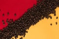 Coffee beans are scattered on a red and yellow paper background close-up, concept, commercial copy space Royalty Free Stock Photo