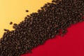 Coffee beans are scattered on a red and yellow paper background close-up, concept, commercial copy space Royalty Free Stock Photo