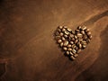 Coffee beans at breakfast shaped in heart on wood grain background.