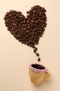 Coffee beans spilled from edible biscuit cup in shape of heart on beige background, top view