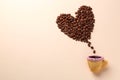 Coffee beans spilled from edible biscuit cup in shape of heart on beige background, top view. Space for text