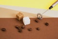 coffee beans, sugar cubes and metal handheld milk steamer on geometric beige and brown background.