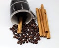 Coffee beans in an upside-down cup and also scattered across the white background at the bottom of the frame. cinnamon near the