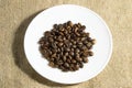 Coffee beans on white saucer. sackcloth background Royalty Free Stock Photo