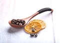 Coffee beans in a wooden spoon and dried oranges on a light wood