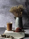 Coffee and biscuits in close up view with grayish background and dried flower at the back