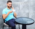 Coffee break brings physical and mental wellbeing. Man sit terrace and drink cappuccino speak phone grey wall background Royalty Free Stock Photo