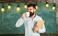 Coffee break concept. Man with beard on calm face in classroom. Teacher in eyeglasses holds book and mug of coffee or Royalty Free Stock Photo