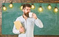 Coffee break concept. Man with beard on calm face in classroom. Teacher in eyeglasses holds book and mug of coffee or Royalty Free Stock Photo