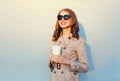 Coffee break! Fashion portrait pretty smiling woman holds cup wearing a coat black sunglasses over sunny grey Royalty Free Stock Photo