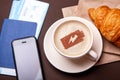 Coffee break, morning coffee. Cup of coffee with foam and croissant with passport and plane ticket