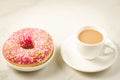 Coffee break: white cup with fresh sugary pink donut/Coffee break: white cup with fresh sugary pink donut on a white marble Royalty Free Stock Photo