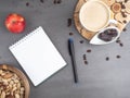 Coffee break in the workplace. White cup of coffee, apple, dates, mix of nuts in wooden bowl, notepad, pen on grey Royalty Free Stock Photo