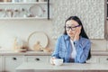 Young tired asian woman freelancer. Sitting at the kitchen table with a cup of coffee, resting Royalty Free Stock Photo