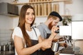 Coffee Business Concept - portrait of lady barista in apron preparing and steaming milk for coffee order with her