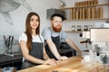 Coffee Business Concept - Positive young bearded man and beautiful attractive lady barista couple in apron looking at Royalty Free Stock Photo