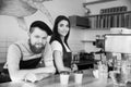 Coffee Business Concept - Positive young bearded man and beautiful attractive lady barista couple in apron looking at Royalty Free Stock Photo