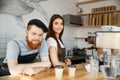 Coffee Business Concept - Positive young bearded man and beautiful attractive lady barista couple in apron looking at Royalty Free Stock Photo