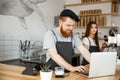 Coffee Business Concept - Young handsome bearded bartende, barista or manager working and planing in laptop at modern Royalty Free Stock Photo