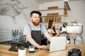 Coffee Business Concept - Young handsome bearded bartende, barista or manager working and planing in laptop at modern Royalty Free Stock Photo