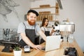 Coffee Business Concept - Young handsome bearded bartender, barista or manager working and planing in laptop at modern Royalty Free Stock Photo