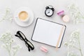 Coffee, cake macaron, notebook, eyeglasses, alarm clock and flower for breakfast on table top view. Woman working desk. Flat lay.