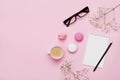 Coffee, cake macaron, notebook, eyeglasses and flower on pink table from above. Female working desk. Cozy breakfast. Flat lay. Royalty Free Stock Photo