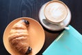 Coffee cappuccino cup, croissant with chocolate and blue colored diary for the year 2023 on wooden table close up with Royalty Free Stock Photo