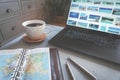 Coffee on concrete table with travel map, pens and laptop with travel destinations as backdrop