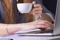Coffee cup in businesswoman`s hand. Young woman working with documents and laptop close-up. Royalty Free Stock Photo