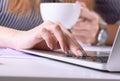 Coffee cup in businesswoman`s hand. Young woman working with documents and laptop close-up. Royalty Free Stock Photo