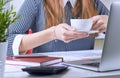 Coffee cup in businesswoman`s hand. Young woman working with documents and laptop close-up. Royalty Free Stock Photo