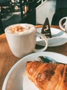 Coffee cup with cream, croissant and chocolate cake on a wooden table Royalty Free Stock Photo