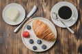 Coffee cup, croissant with berries in white bowl and butter knife on wooden table. Top view. Healthy breakfast with fresh berries Royalty Free Stock Photo