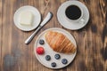 Coffee cup, croissant with berries in white bowl and butter knife on wooden table. Top view. Healthy breakfast with fresh berries Royalty Free Stock Photo