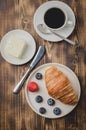 Coffee cup, croissant with berries in white bowl and butter knife on wooden table. Top view. Healthy breakfast with fresh berries Royalty Free Stock Photo