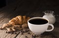 Coffee cup with croissant, bread, bakery or breakfast cake laying on a wooden table on a black needle background Royalty Free Stock Photo