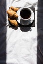 Coffee cup and croissants on the bed in morning sunlight. Trendy still life with interesting shadow.