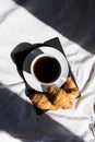 Coffee cup and croissants on the bed in morning sunlight. Trendy still life with interesting shadow.