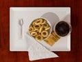 Coffee cup, double glass coffee cup with bowl of cookies, spoon, napkin and sugar sachets on white ceramic tray on wooden table