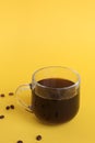 Glass cup with black coffee on yellow background