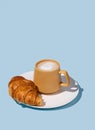 Coffee cup and fresh croissant on a white plate on a blue background Royalty Free Stock Photo