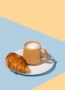 Coffee cup and fresh croissant on a white plate on a blue and yellow background Royalty Free Stock Photo