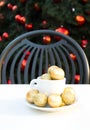 Coffee cup with golden Christmas balls inside. Coffee pair on white table, grey chair and new year tree with red toys in Royalty Free Stock Photo